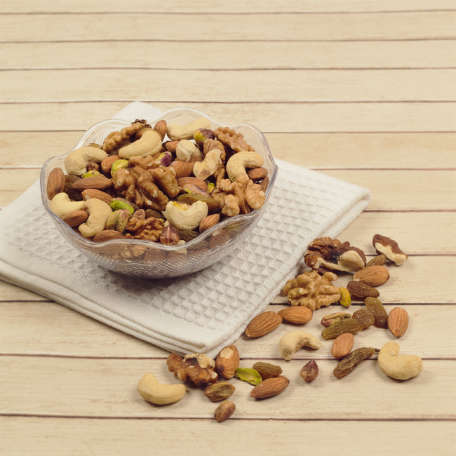 A glass bowl of mixed nuts, including almonds, cashews, and walnuts, on a wooden table with a cloth. - Types of Popular Dry Fruits in Pakistan for Gifting
