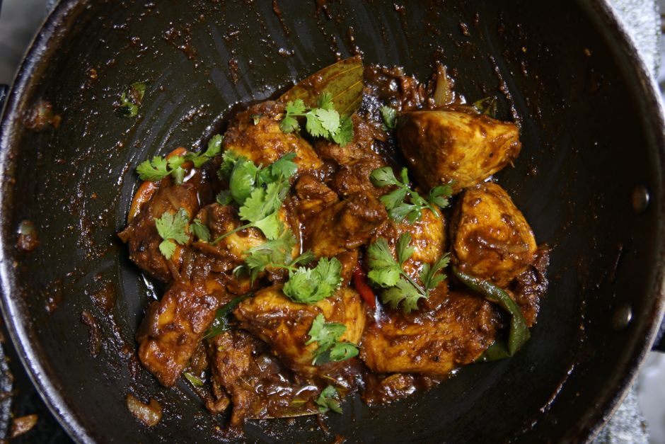 Bhuna curry in a wok with meat and green garnish