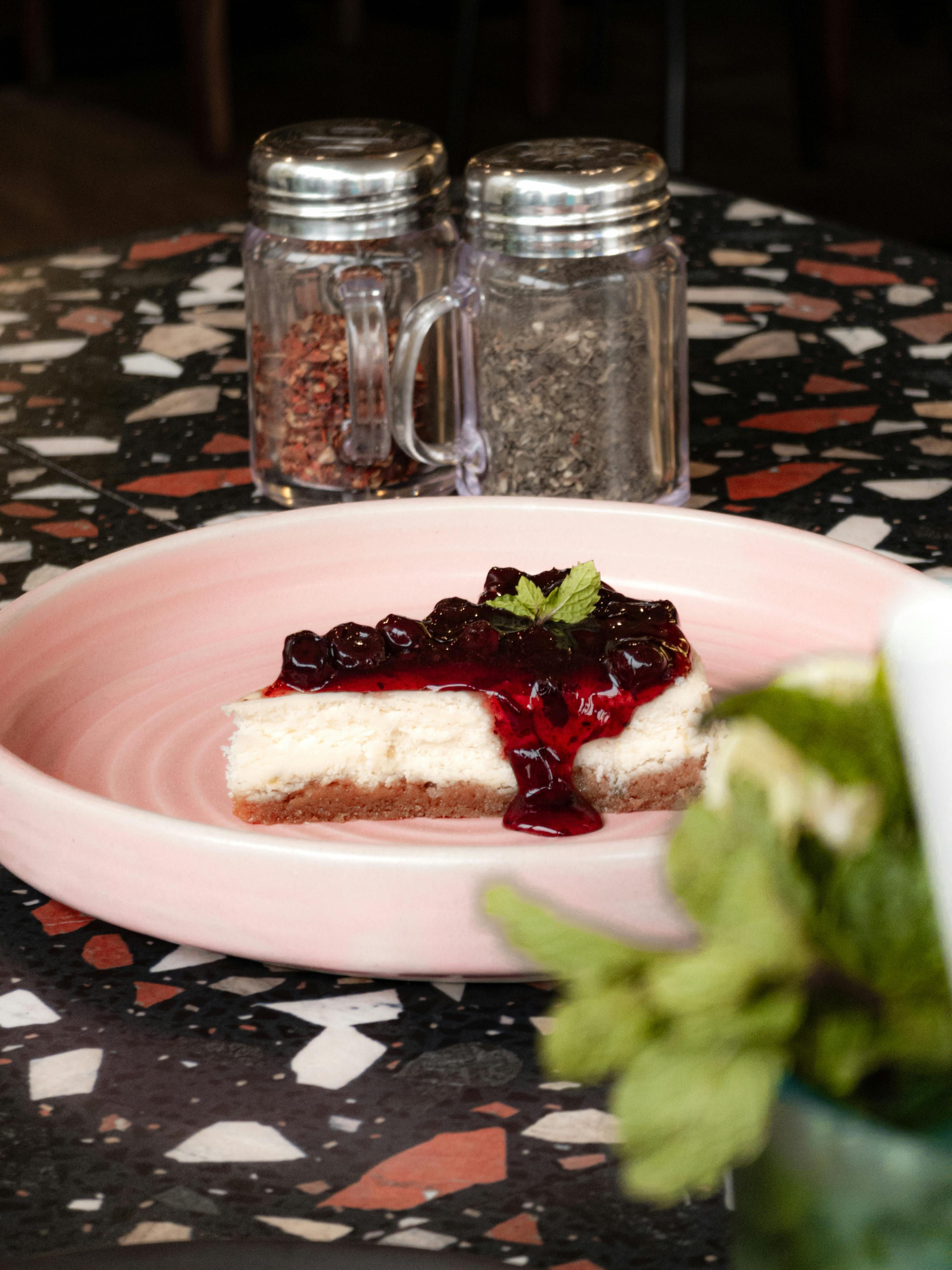 Delicious cherry cheesecake slice with berry topping on pink plate in café setting.