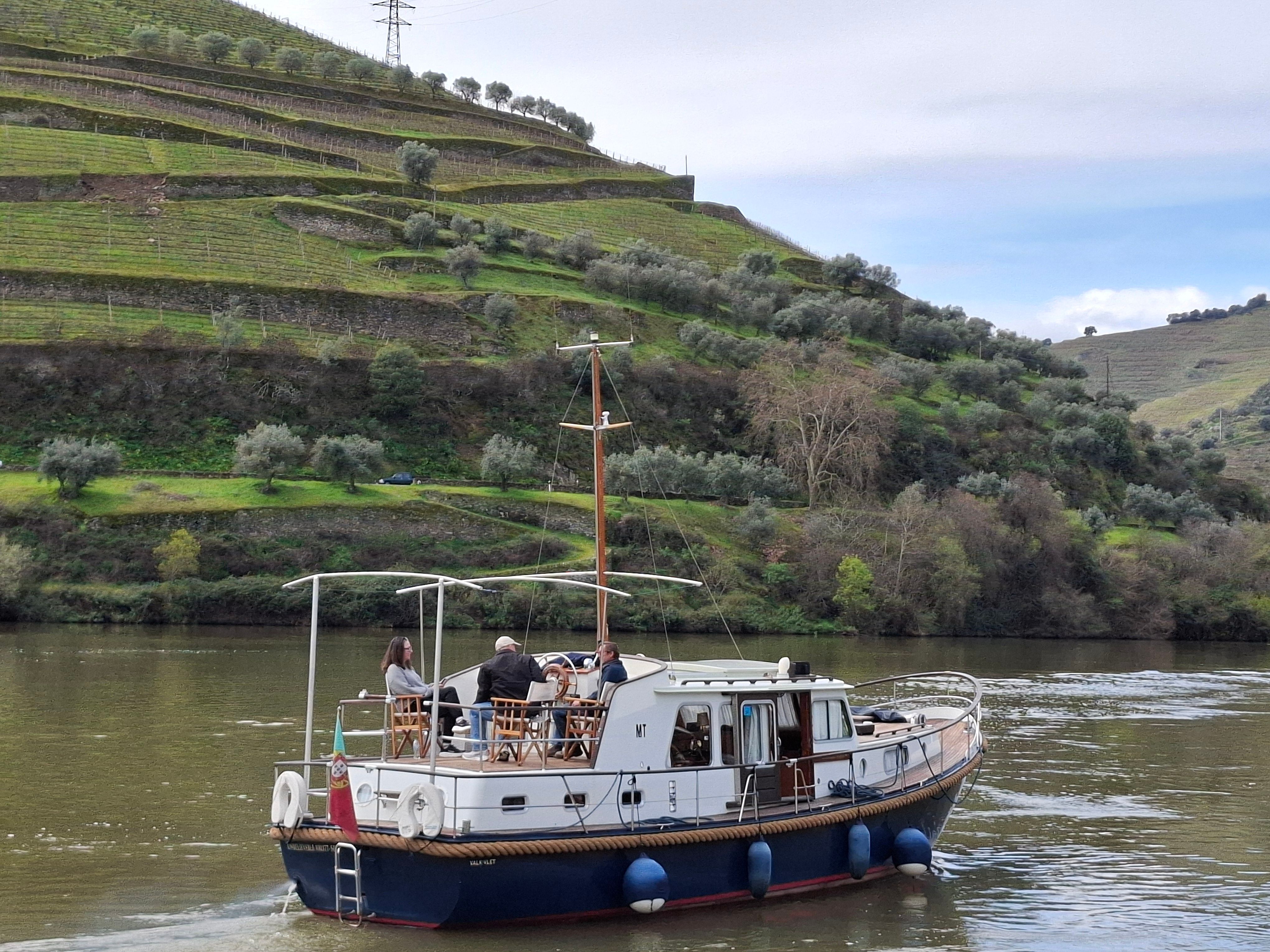 Vineyards and a traditional Rabelo boat on the Douro River in Portugal, illustrating a wine tour.