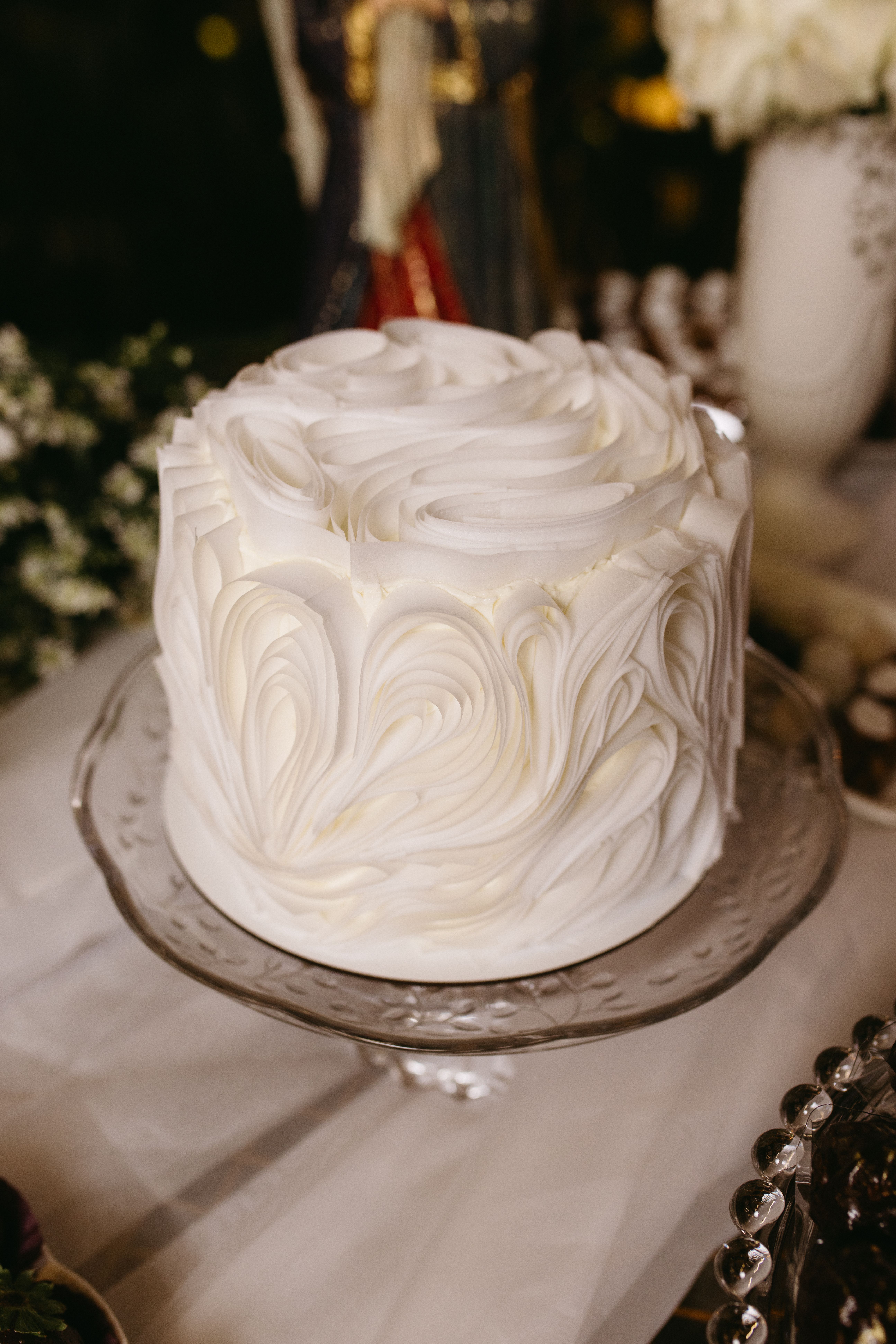 A beautifully decorated white frosted cake on a glass stand, perfect for weddings or celebrations.
