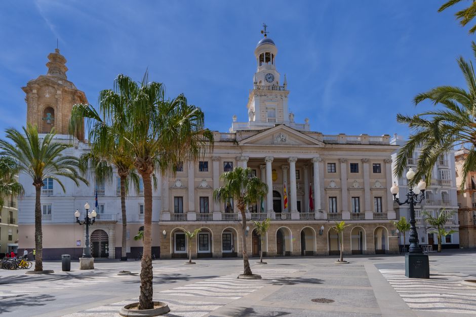 Elegante Ayuntamiento en Cádiz, con arquitectura histórica y palmeras bajo un cielo azul claro.