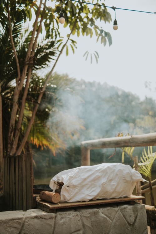 Free A cozy outdoor rest area with a campfire setup and seating, shaded by palm trees and string lights. Stock Photo