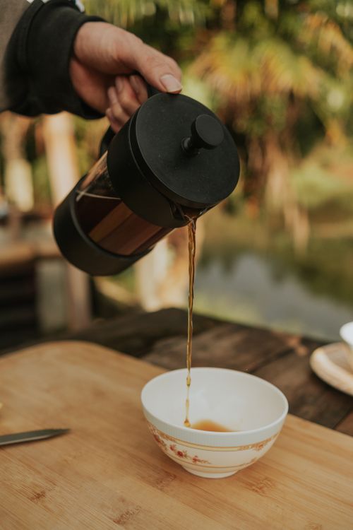 Free A hand pouring freshly brewed coffee from a French press into a cup outdoors on a warm day. Stock Photo