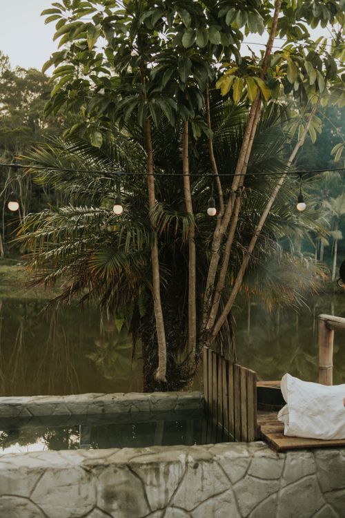 Free A tranquil outdoor jacuzzi near a tropical lake with string lights, creating a peaceful atmosphere. Stock Photo