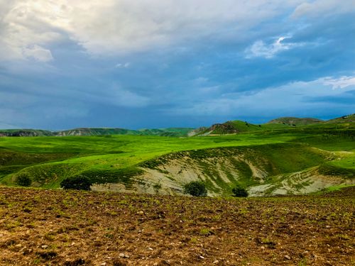 Free Expansive green hills beneath a dynamic, cloudy sky, capturing the beauty of nature. Stock Photo