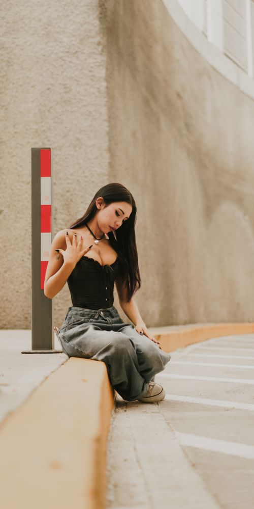 Free Stylish young woman in casual outfit sitting on a curbside in an urban setting, lost in thought. Stock Photo