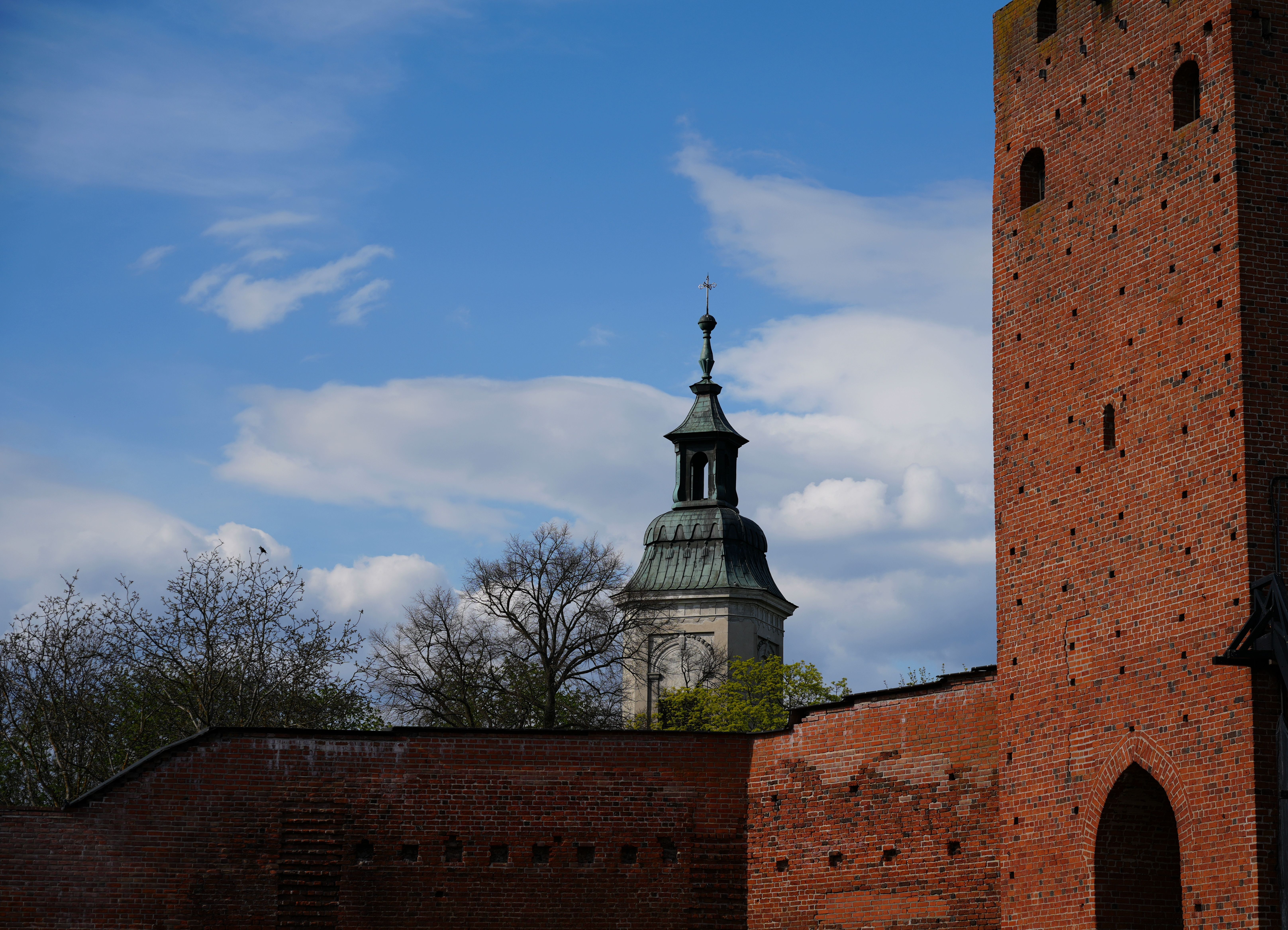 Brick castle tower and church steeple in Masovian Voivodeship, Poland set against a clear blue sky.