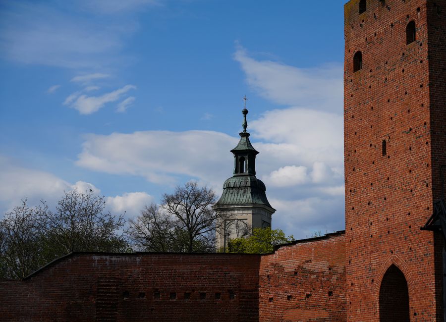 Brick castle tower and church steeple in Masovian Voivodeship, Poland set against a clear blue sky.