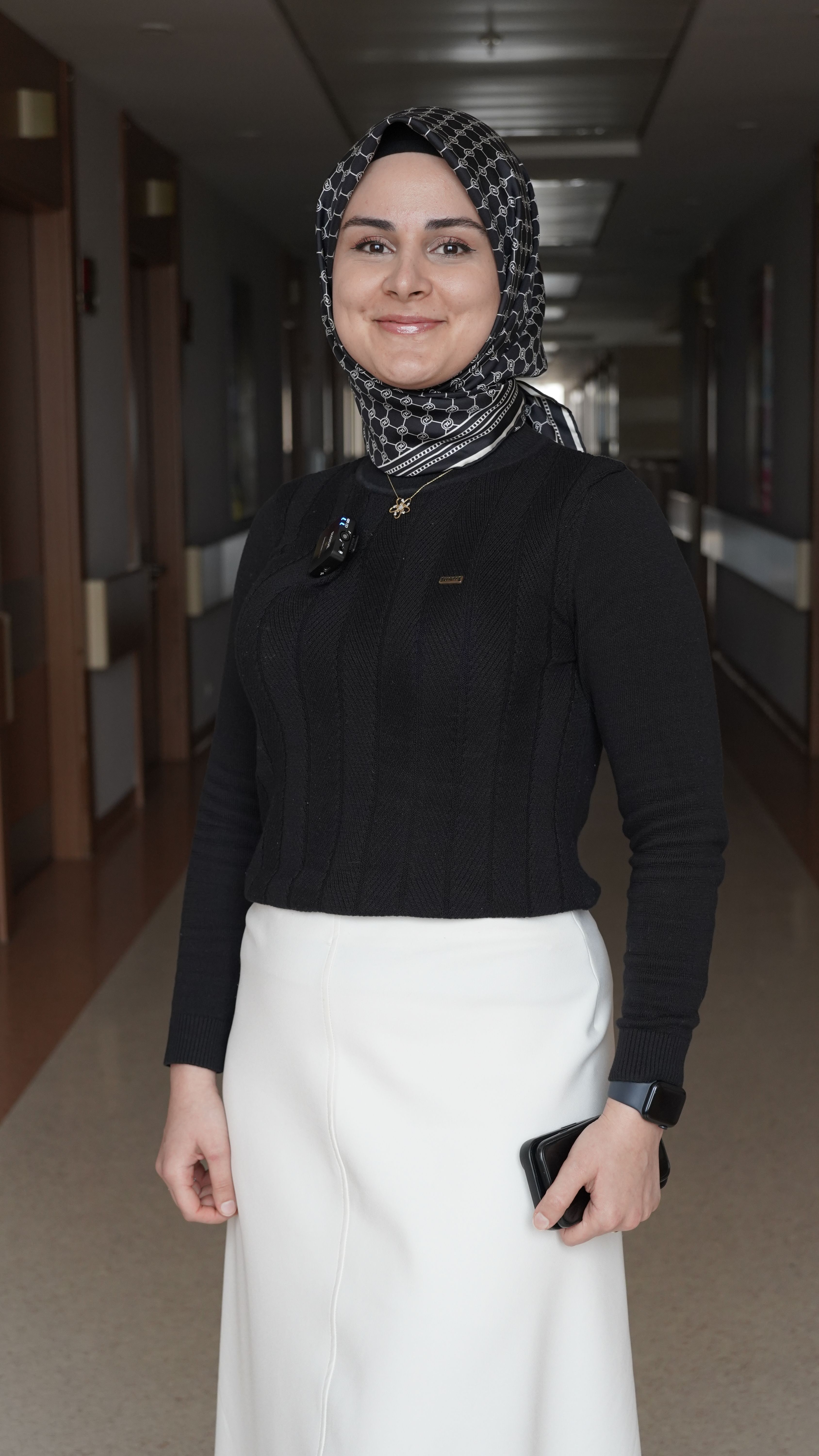 Smiling woman wearing hijab and business outfit standing indoors, exuding confidence.