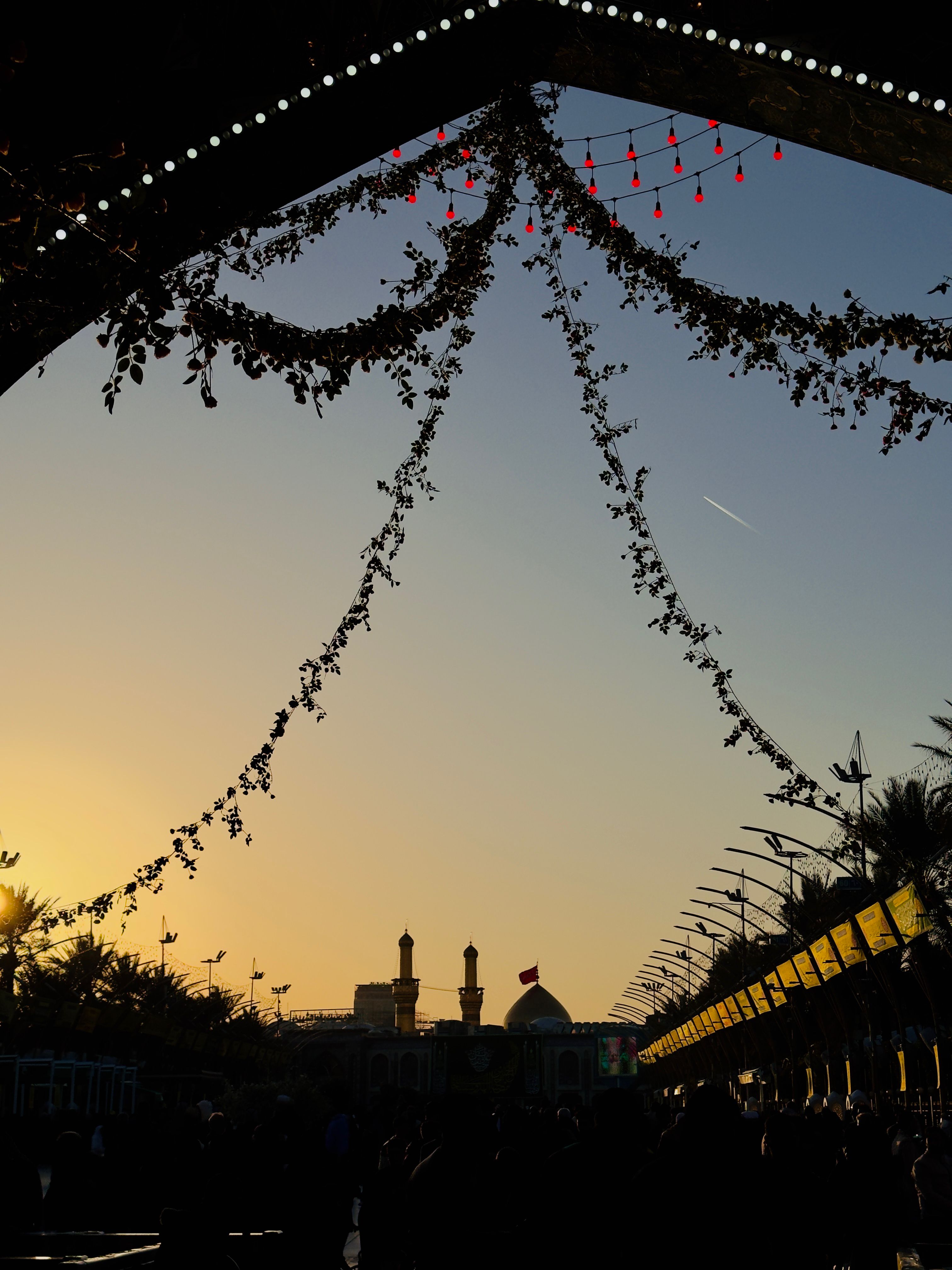 A silhouette of a mosque adorned with lights and foliage during a beautiful golden sunset.