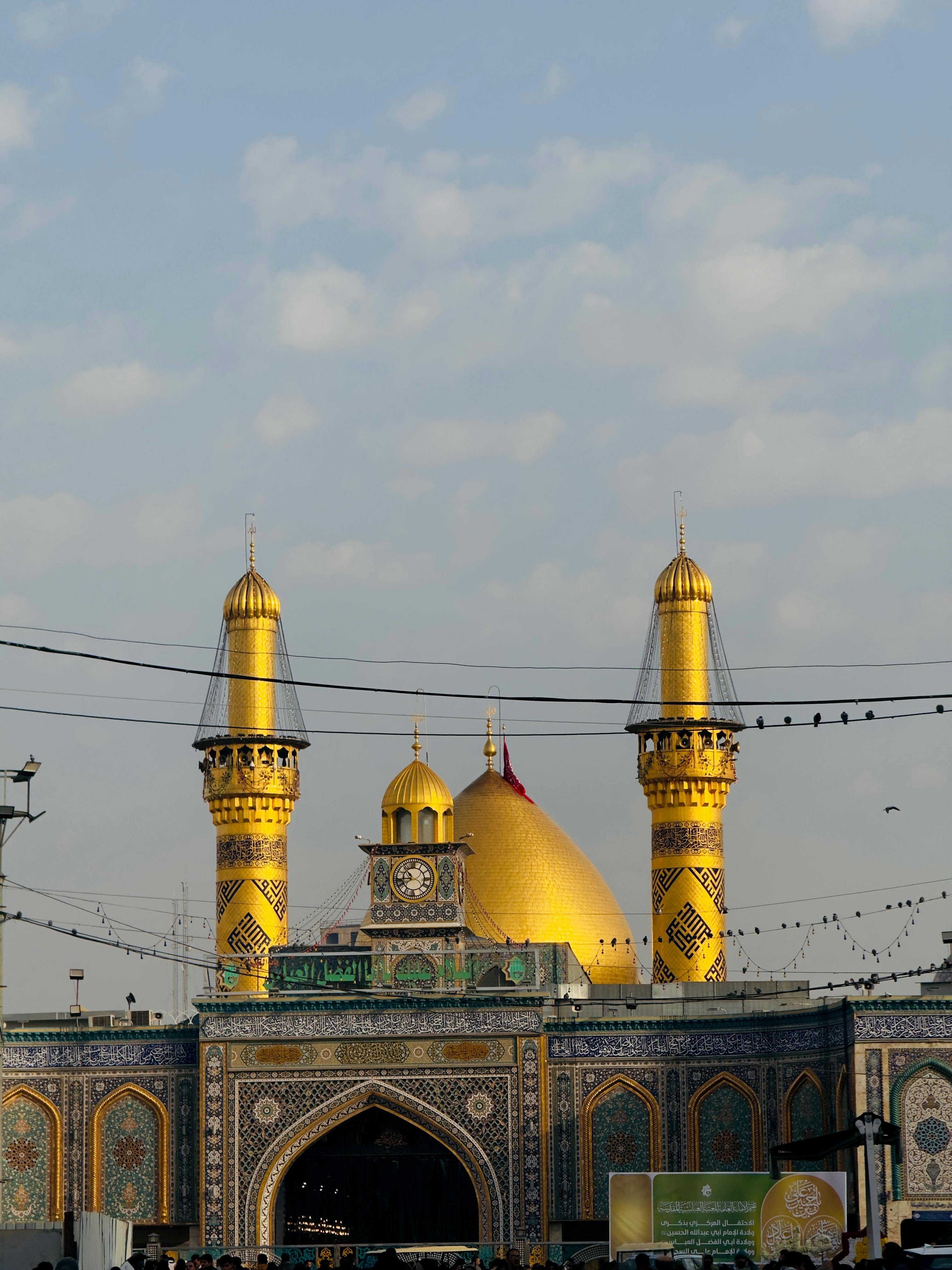 Imam Ali Mosque's golden domes and minarets under a blue sky in Najaf, Iraq.