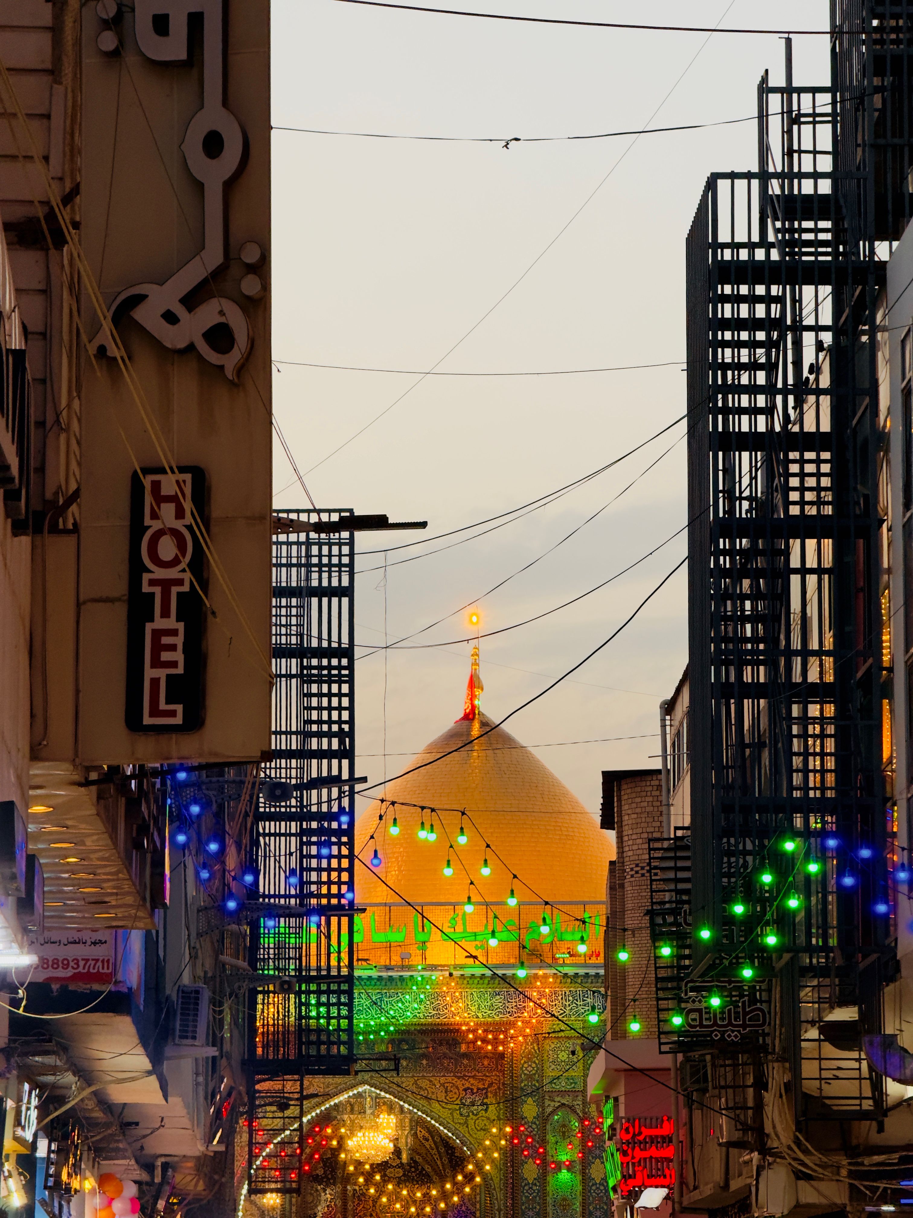 Colorful night market with a view of a golden dome, vibrant lights, and bustling atmosphere.
