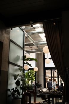 A stylish cafe interior with large windows, hanging lights, and indoor plants, capturing an ambient urban atmosphere.