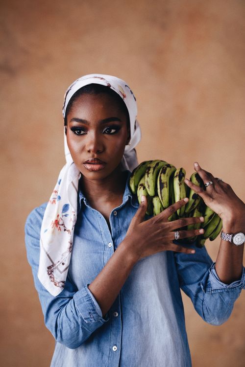 Free Young woman in hijab holding a bunch of bananas against a neutral backdrop. Stock Photo