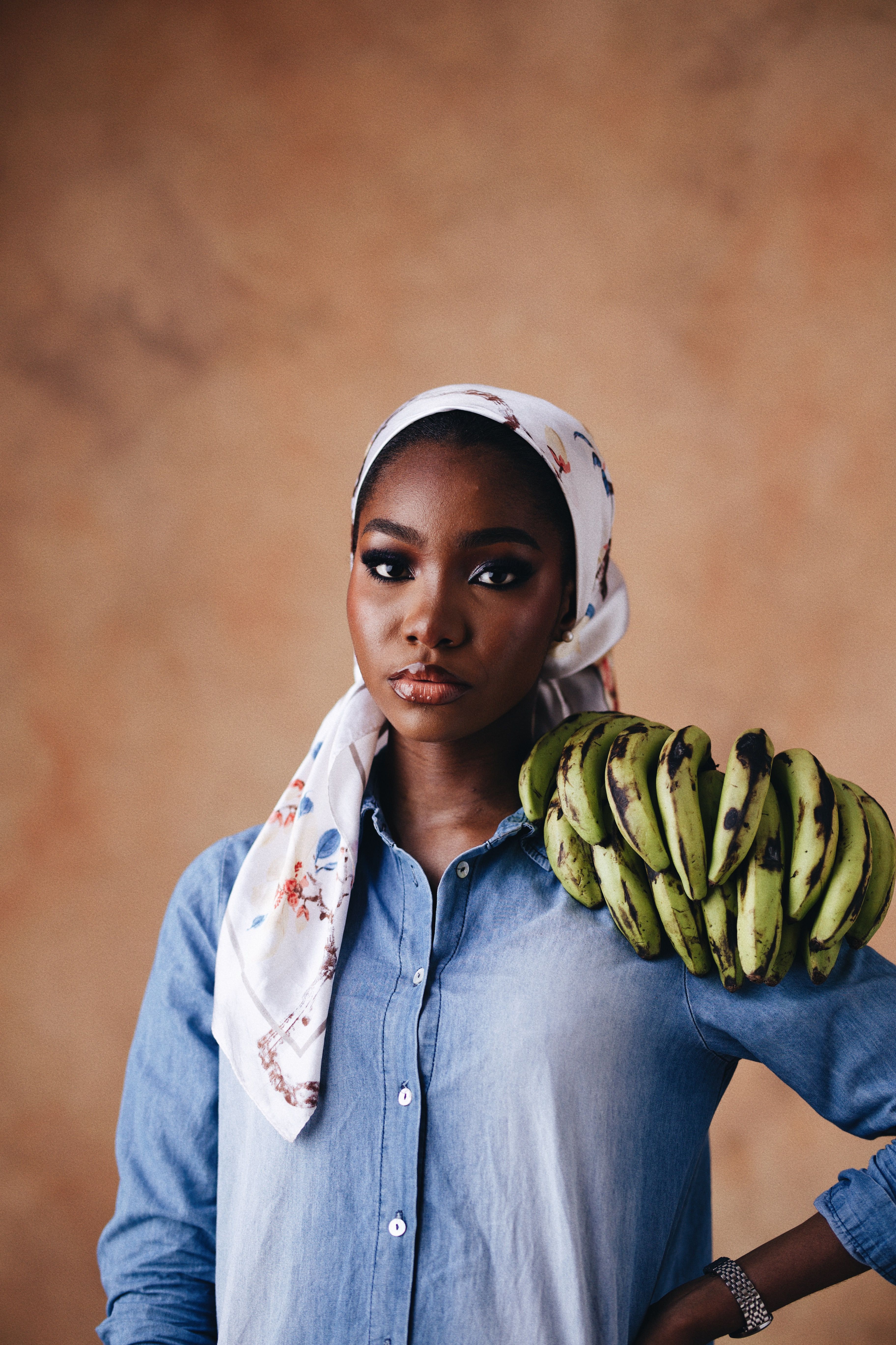 Young woman holding a bunch of green bananas against a neutral background, conveying natural beauty.