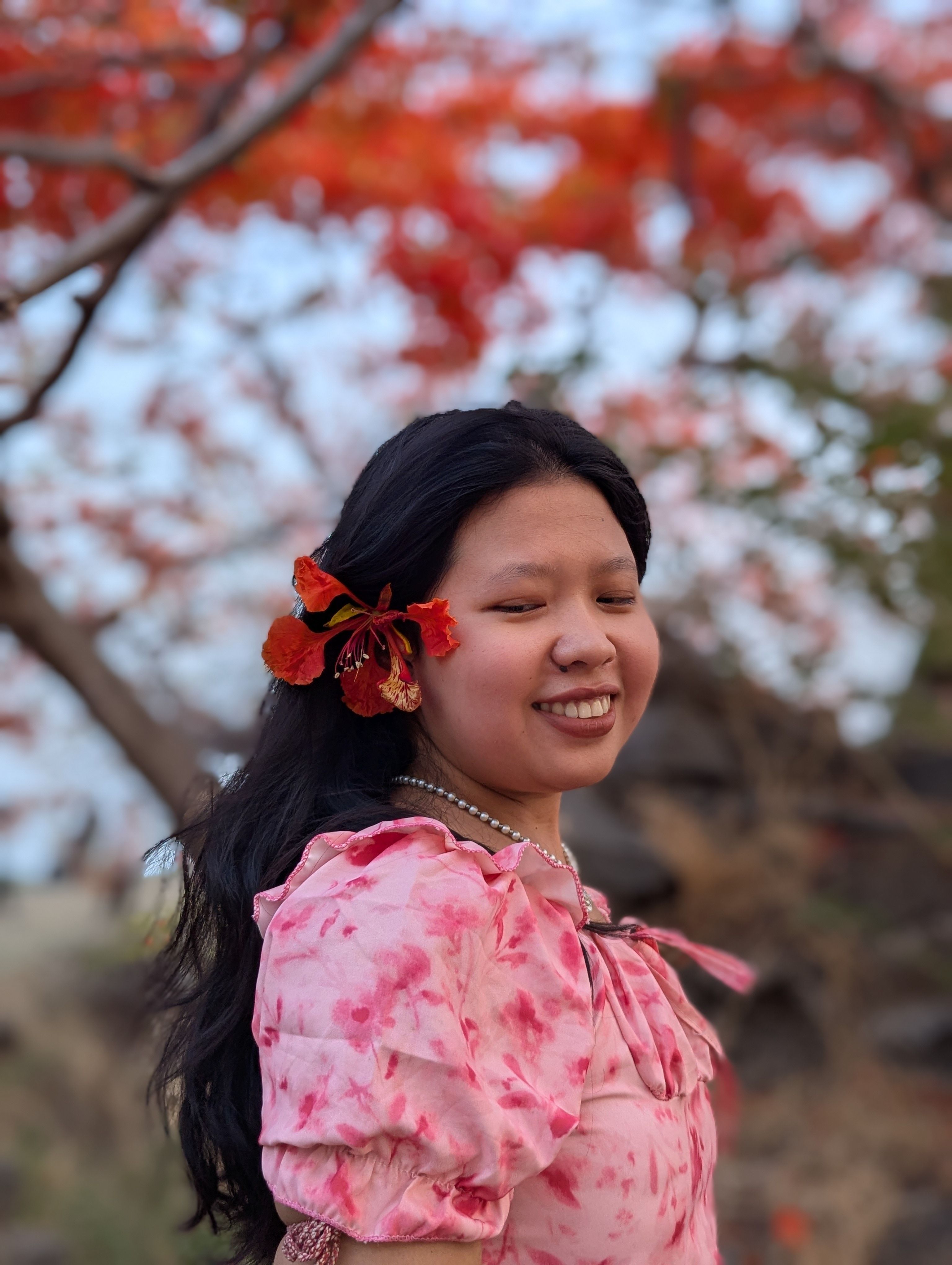 Portrait of a smiling young woman in a pink dress with vibrant red flowers in the background.