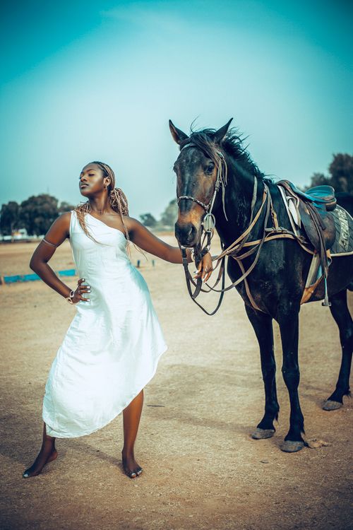 Free Confident woman in a flowing white dress poses gracefully with a dark horse. Stock Photo