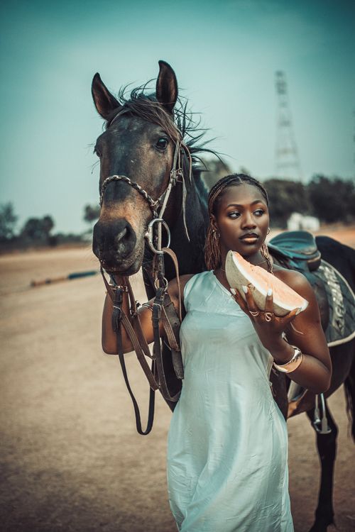 Free A woman in a white dress stands with a horse in an open sandy field, enjoying a summer day. Stock Photo
