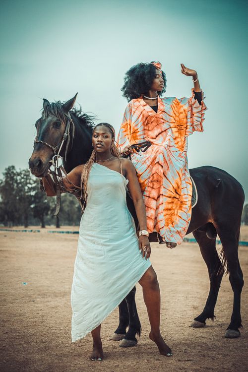 Free Two women interact with a horse in an open field, showcasing fashion and grace. Stock Photo