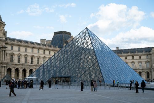 Free The iconic glass pyramid of the Louvre Museum in Paris with visitors on a clear day. Stock Photo