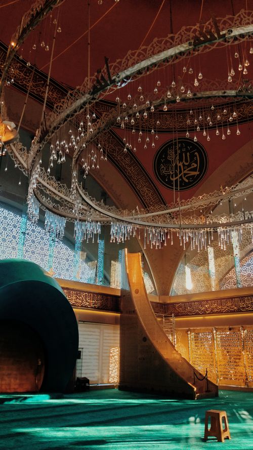 Free Beautifully lit mosque interior featuring intricate chandeliers and Arabic calligraphy. Stock Photo