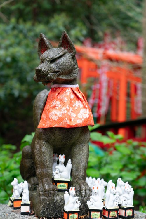 Free A fox statue adorned with a red bib, surrounded by miniature fox figurines in Kamakura, Japan. Stock Photo