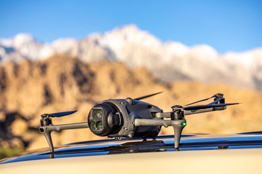 A drone resting on a car roof with snow-capped mountains, showcasing outdoor technology in a scenic setting.