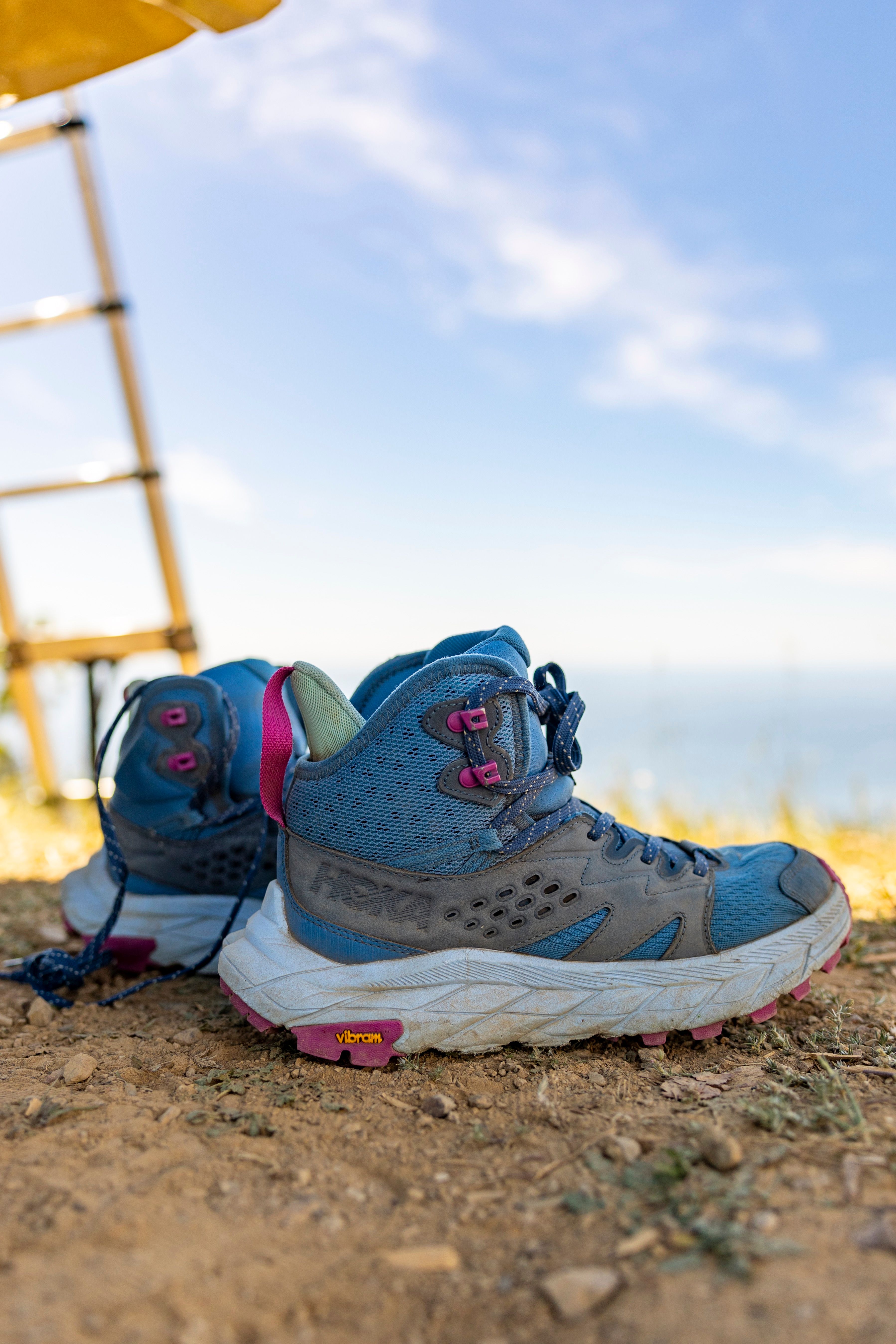 A pair of hiking boots on a trail overlooking the ocean on a sunny day.