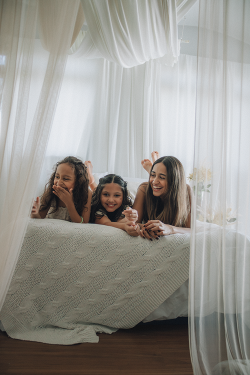 Free Three family members enjoy a cozy time together on a bed with sheer curtains. Stock Photo