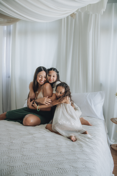 Free A mother lovingly embraces her two daughters on a bed, creating a warm family moment. Stock Photo