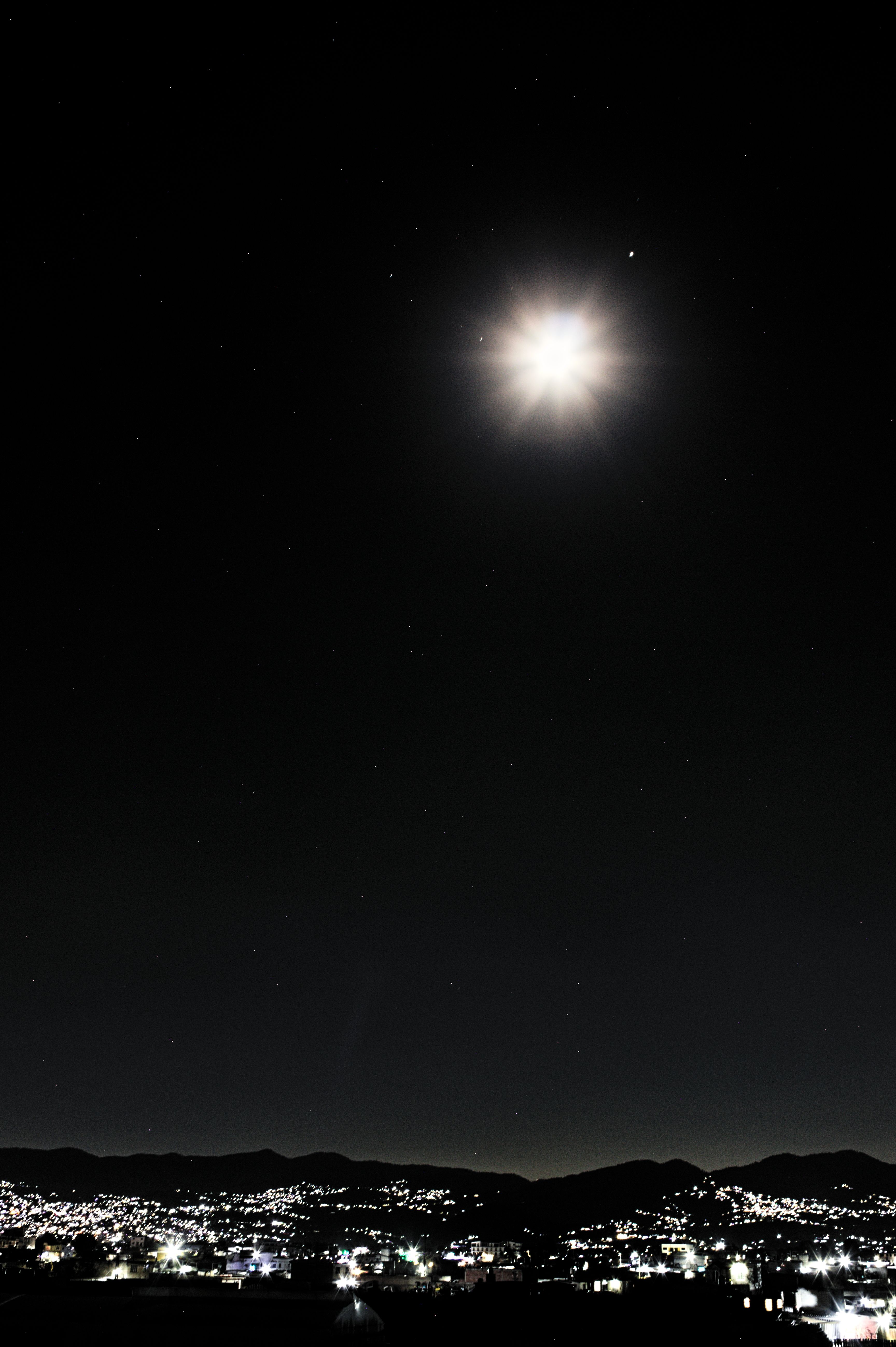 Fotomural Una vista impresionante de una luna llena luminosa que ilumina el extenso horizonte de la ciudad bajo un cielo nocturno estrellado.