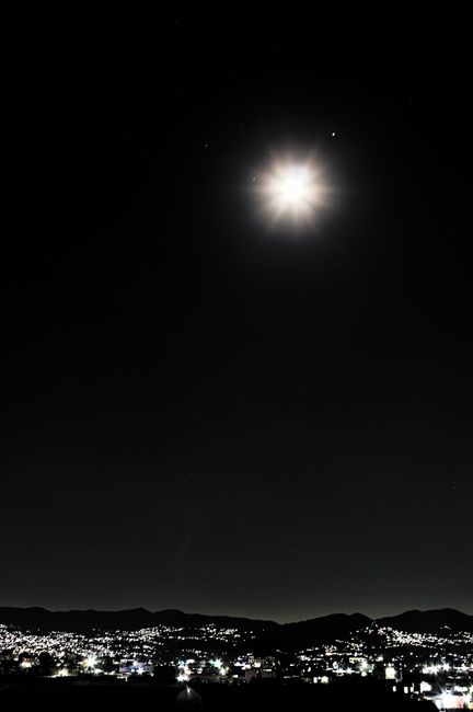 Fotomural Una vista impresionante de una luna llena luminosa que ilumina el extenso horizonte de la ciudad bajo un cielo nocturno estrellado.