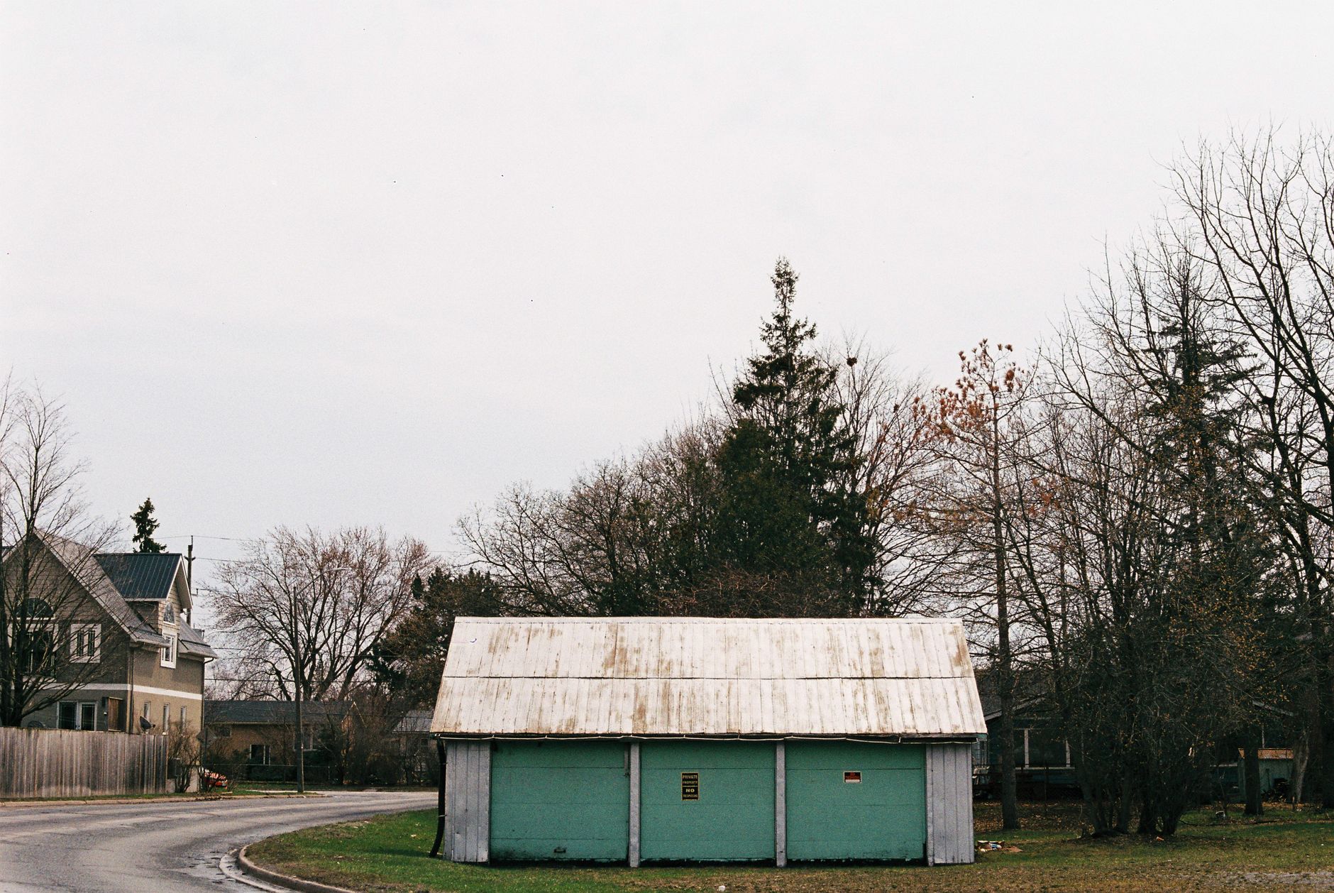 A snow-dusted suburban neighborhood in winter, with bare trees surrounding quiet residential homes under an overcast sky.