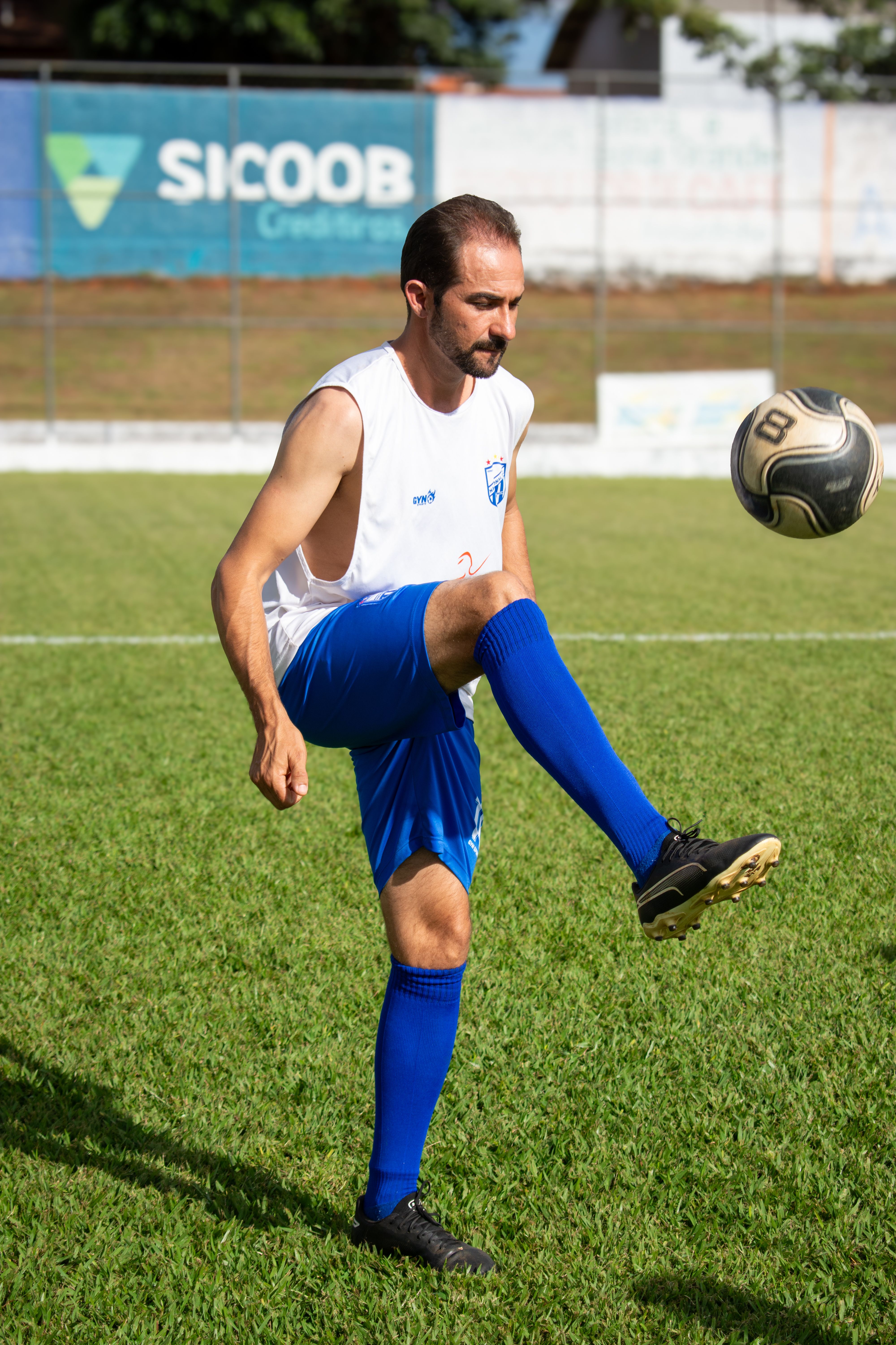 Man in blue uniform practicing soccer juggling on a grass field in daylight.