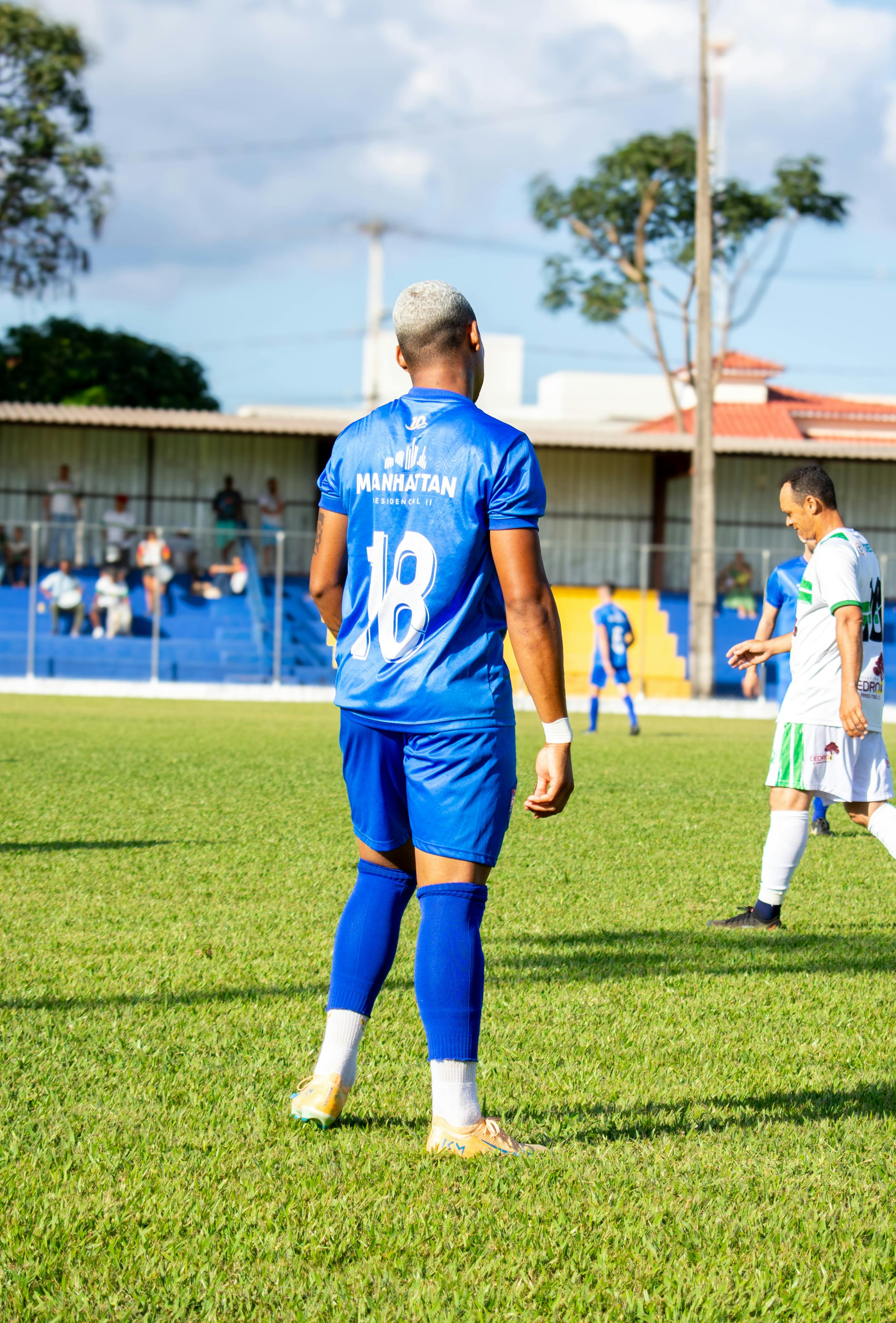 A soccer player in a blue uniform with number 18 plays outdoors on a sunny day.