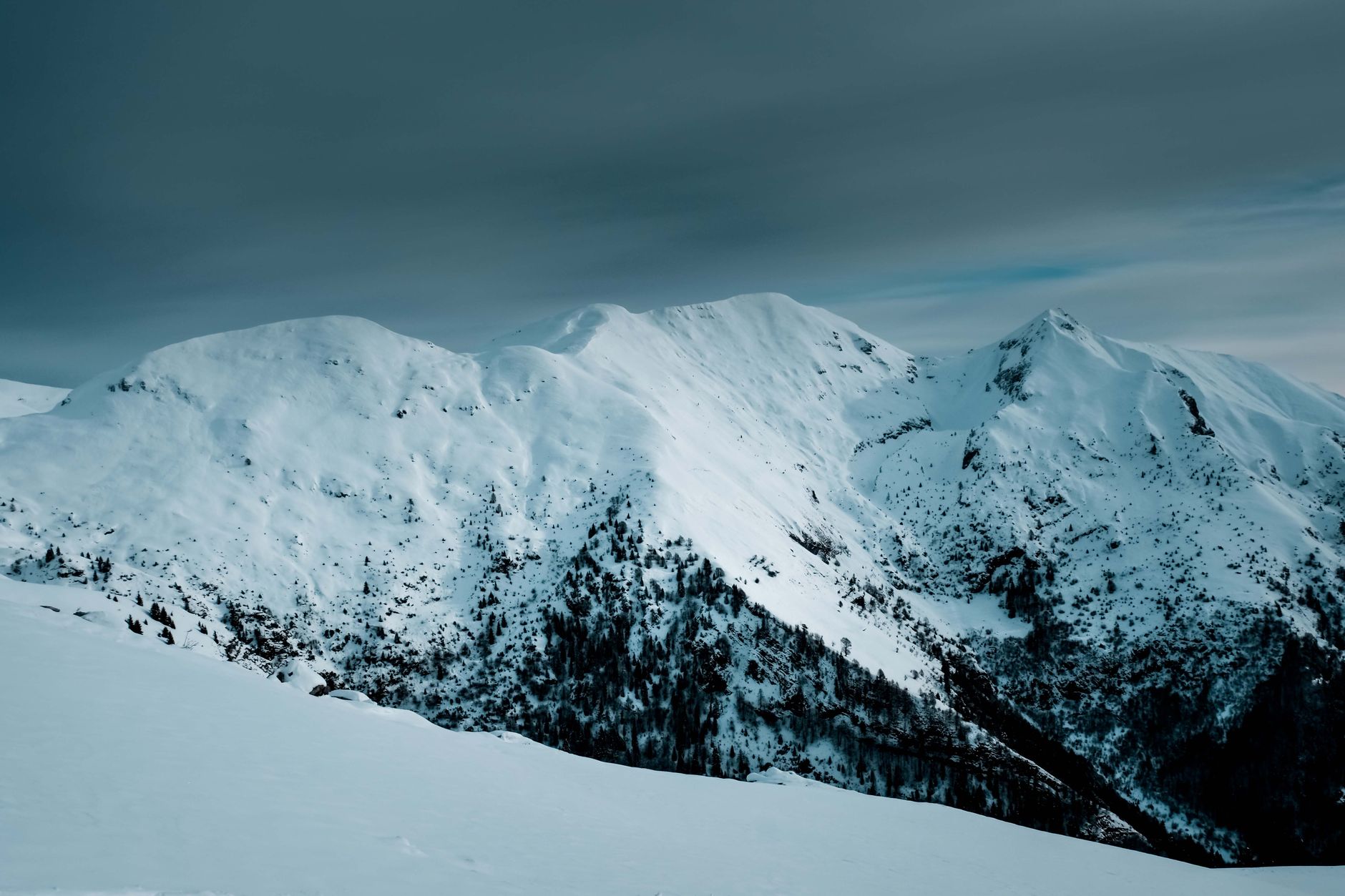 Snow-capped mountain range under a moody winter sky, showing how elevation changes snow accumulation.