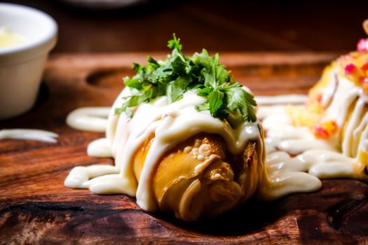 Delicious stuffed pastry topped with creamy sauce and fresh herbs on a wooden board.