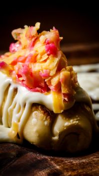 Close-up of a gourmet dessert roll topped with vibrant shredded vegetables and icing on a wooden surface.