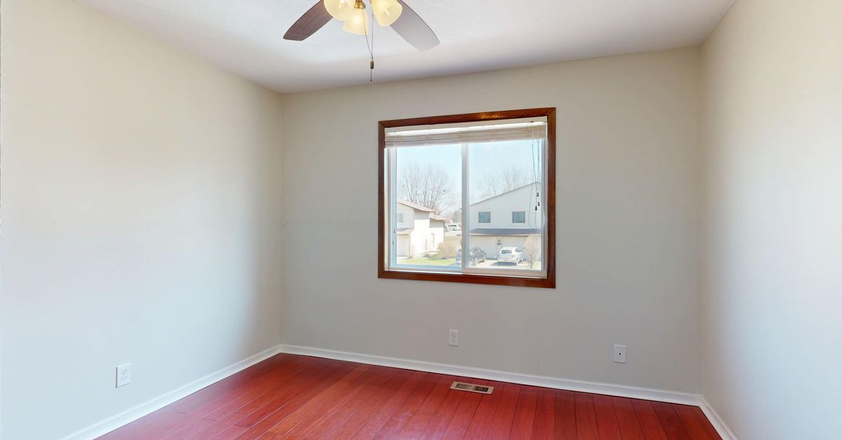 Spacious empty room with wooden flooring, window view, and ceiling fan.
