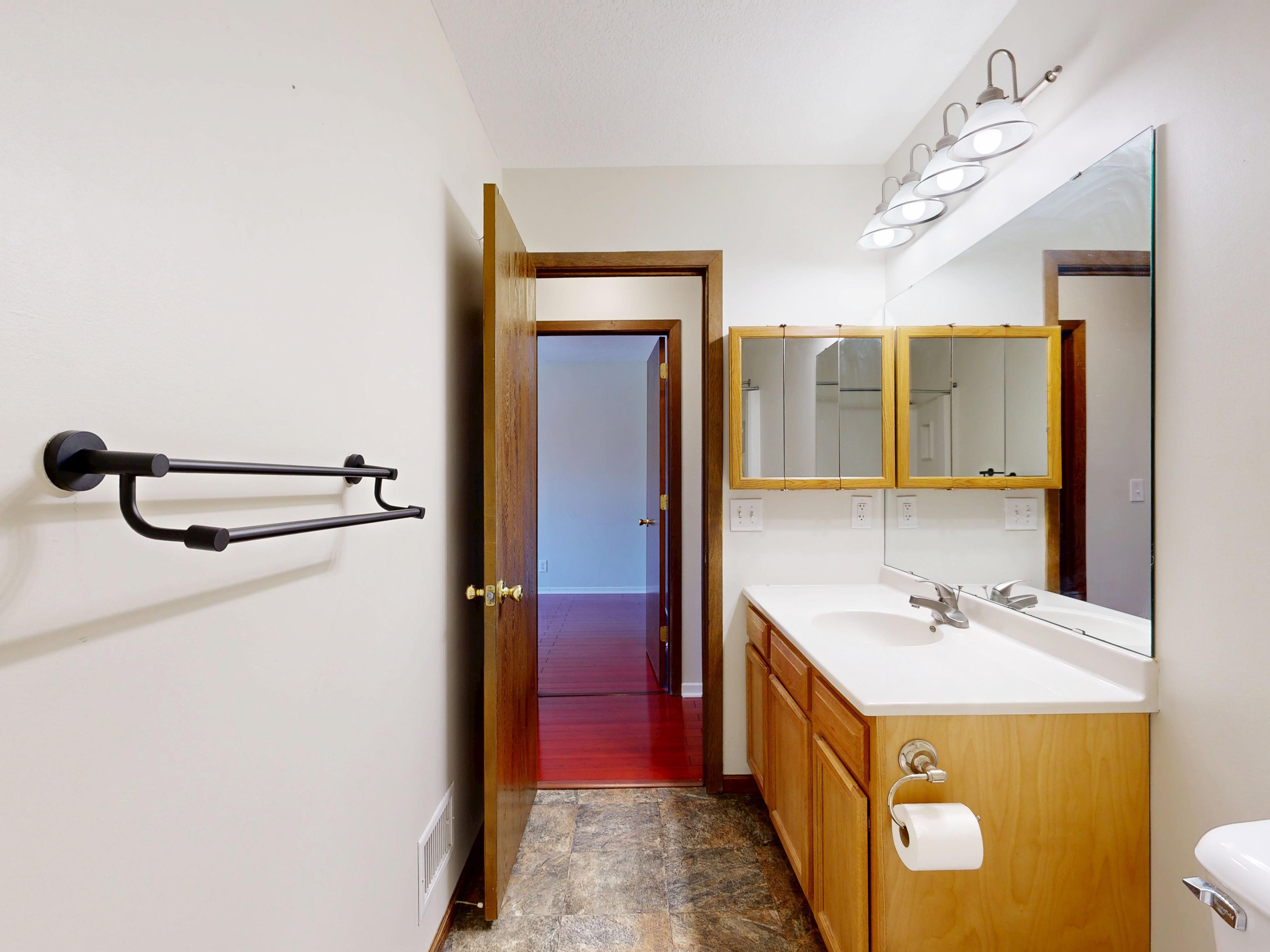 A bright, modern bathroom with wooden cabinetry, mirror, and towel rack.