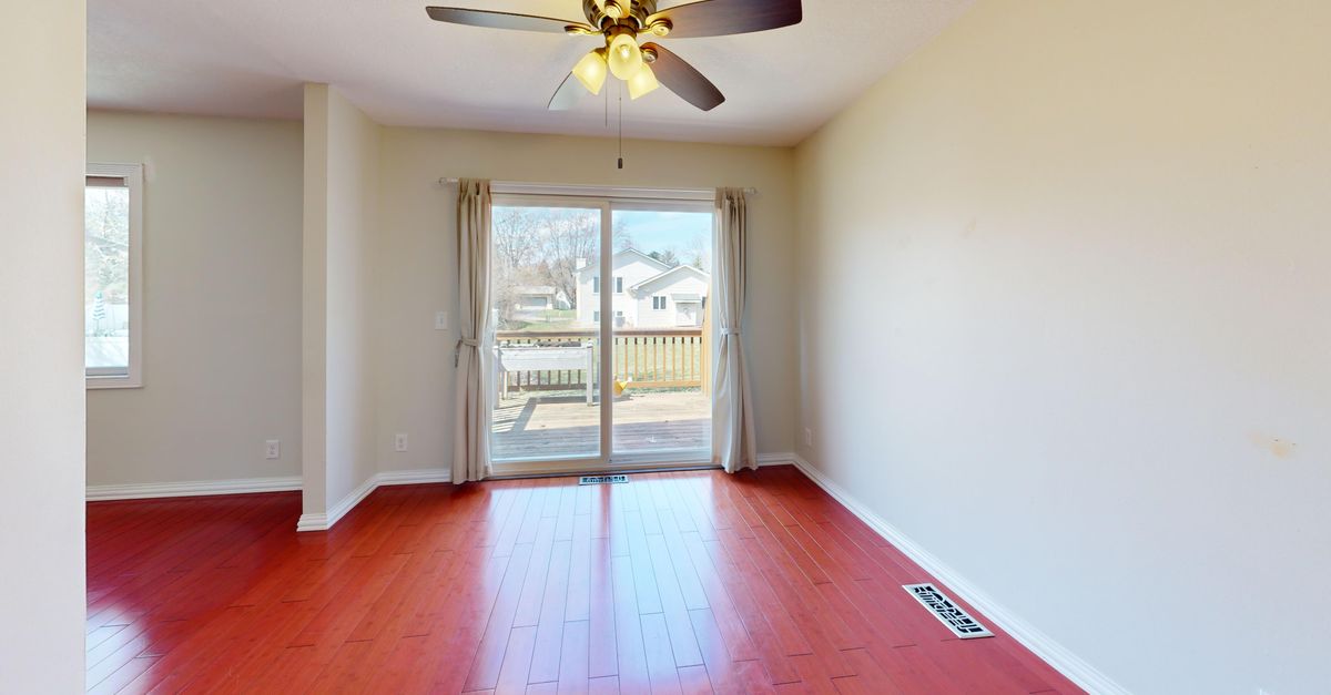 Spacious empty room with red wooden flooring, ceiling fan, and patio view.