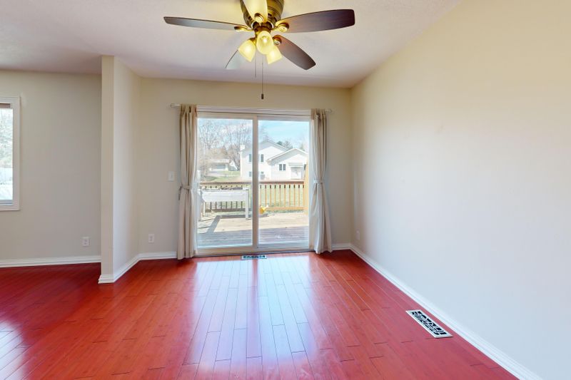 Spacious empty room with red wooden flooring, ceiling fan, and patio view.