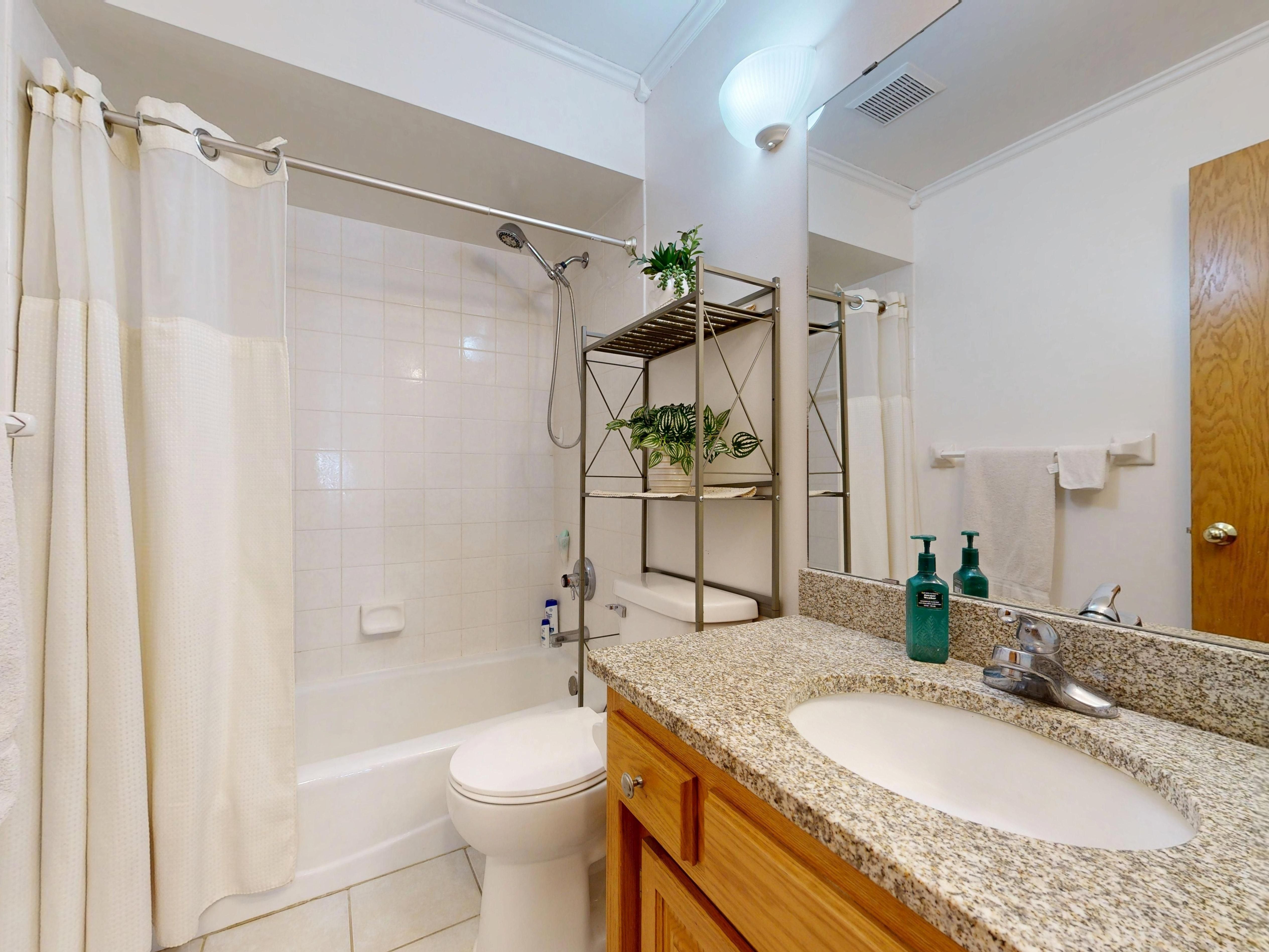 Bright bathroom with granite countertop and shower, depicting modern design and cleanliness.