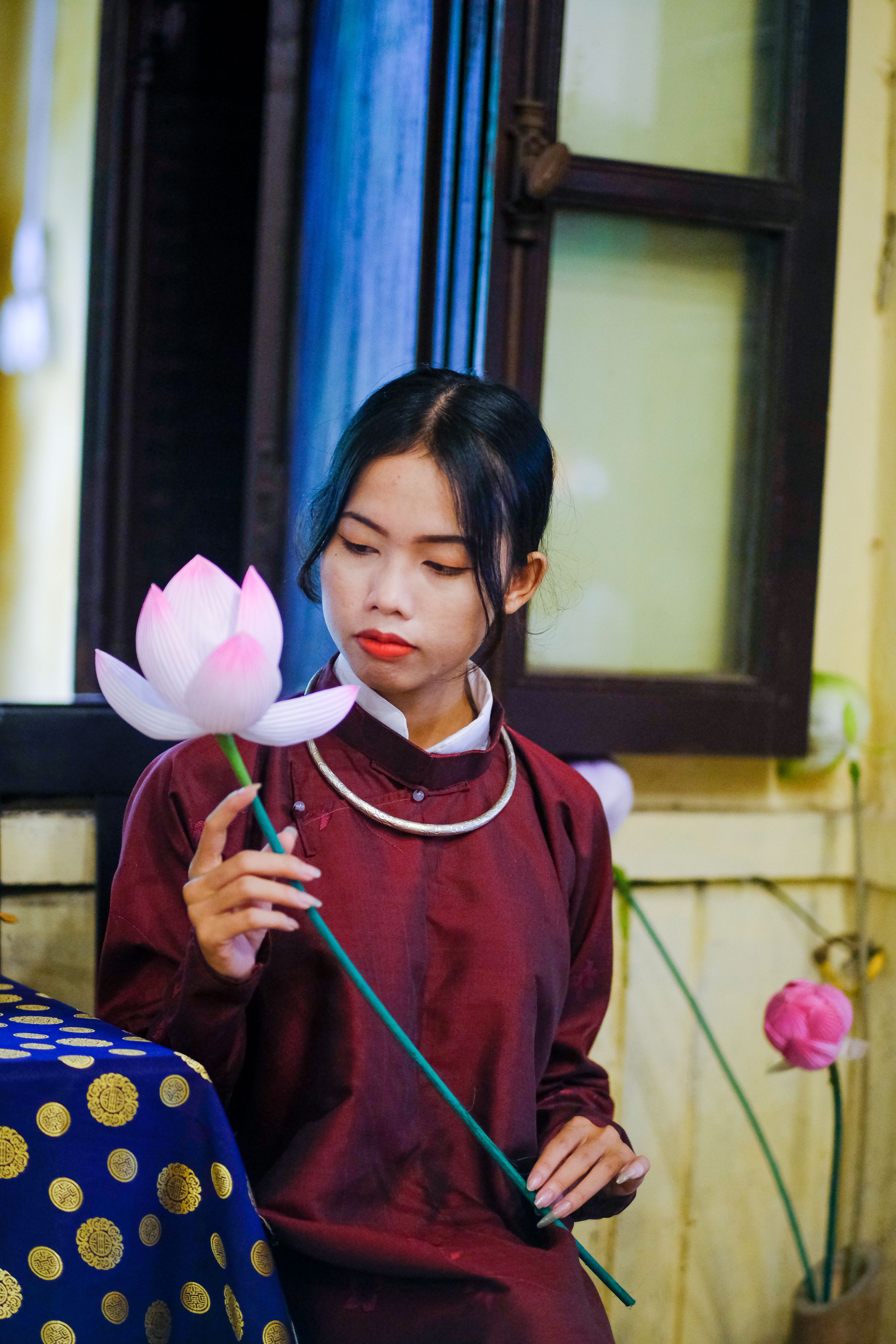 A woman in traditional attire holds a lotus flower in Hue, Vietnam, showcasing Vietnamese culture.
