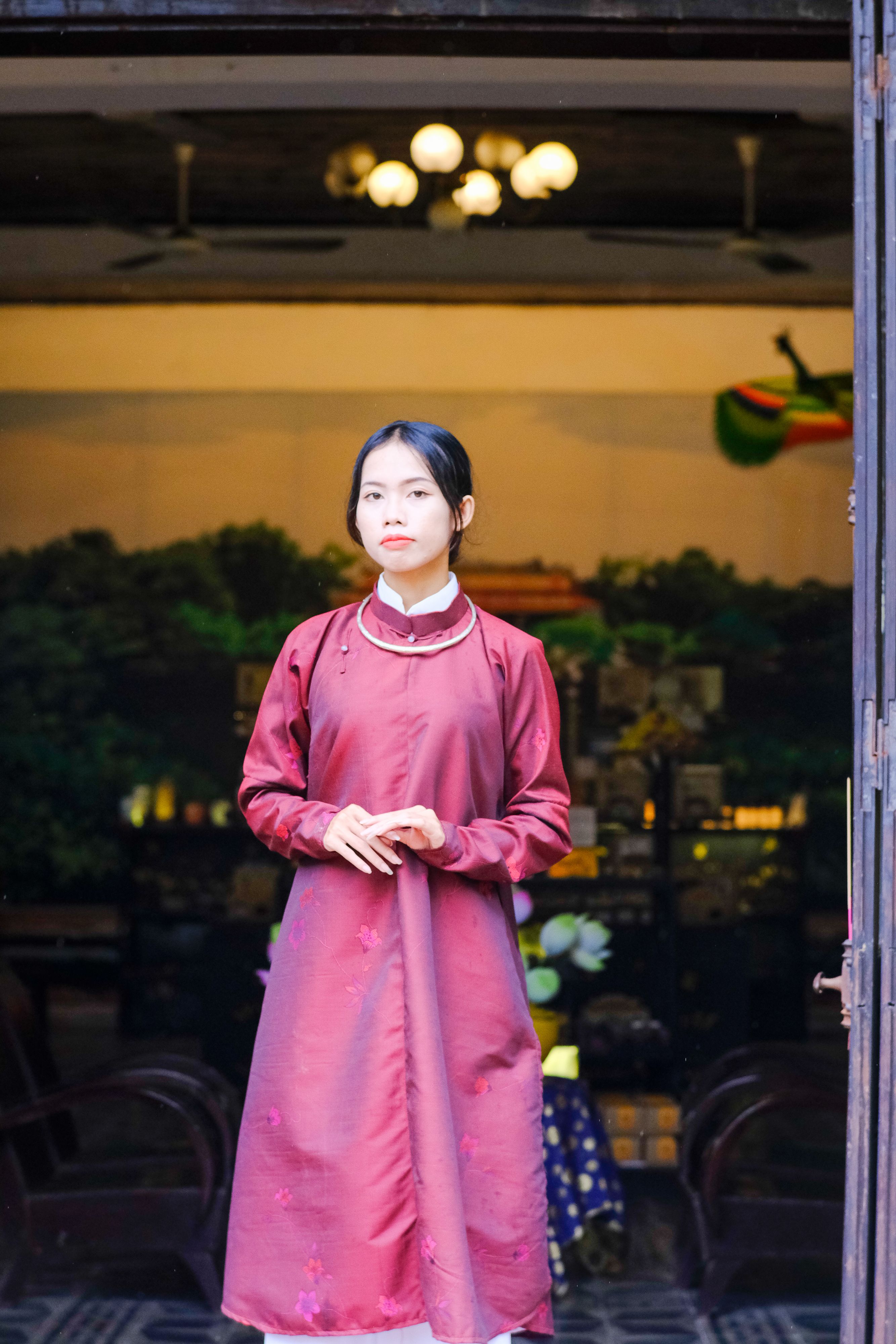 A portrait of a Vietnamese woman in traditional attire standing in a doorway in Hue, Vietnam.