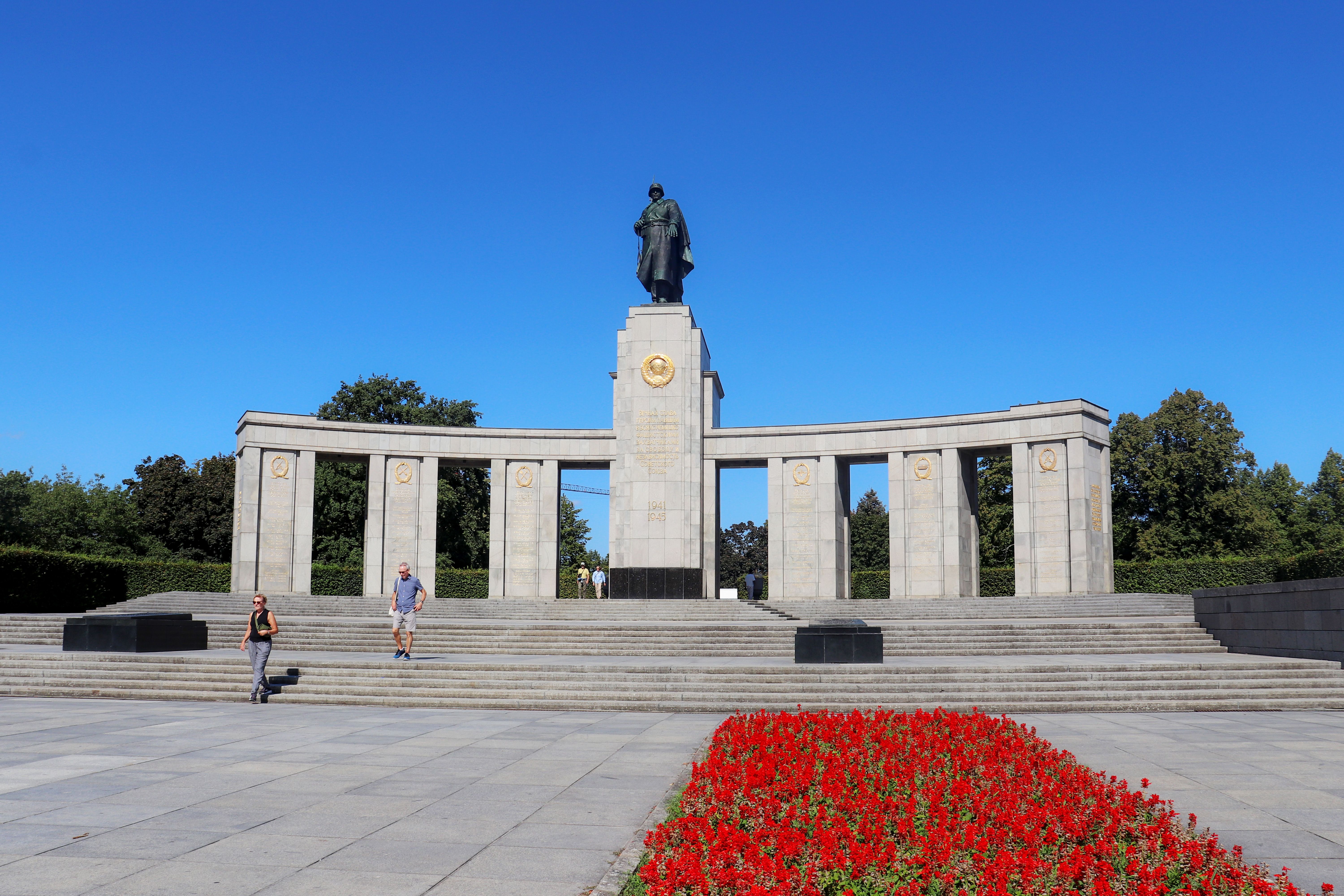 Kostenlos Das sowjetische Ehrenmal in Berlin, Deutschland, mit leuchtend roten Blumen unter klarem blauen Himmel. Stock-Foto
