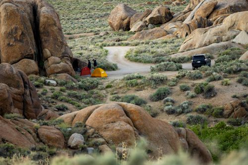 Free Outdoor camping scene in a desert landscape with two tents, a car, and rocky formations. Stock Photo