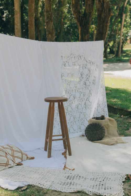 Free Vintage bohemian outdoor setup with stool and lace backdrop in sunny park setting. Stock Photo