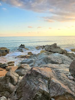 Serene beach scene with rocks and a stunning sunset over calm ocean waters.